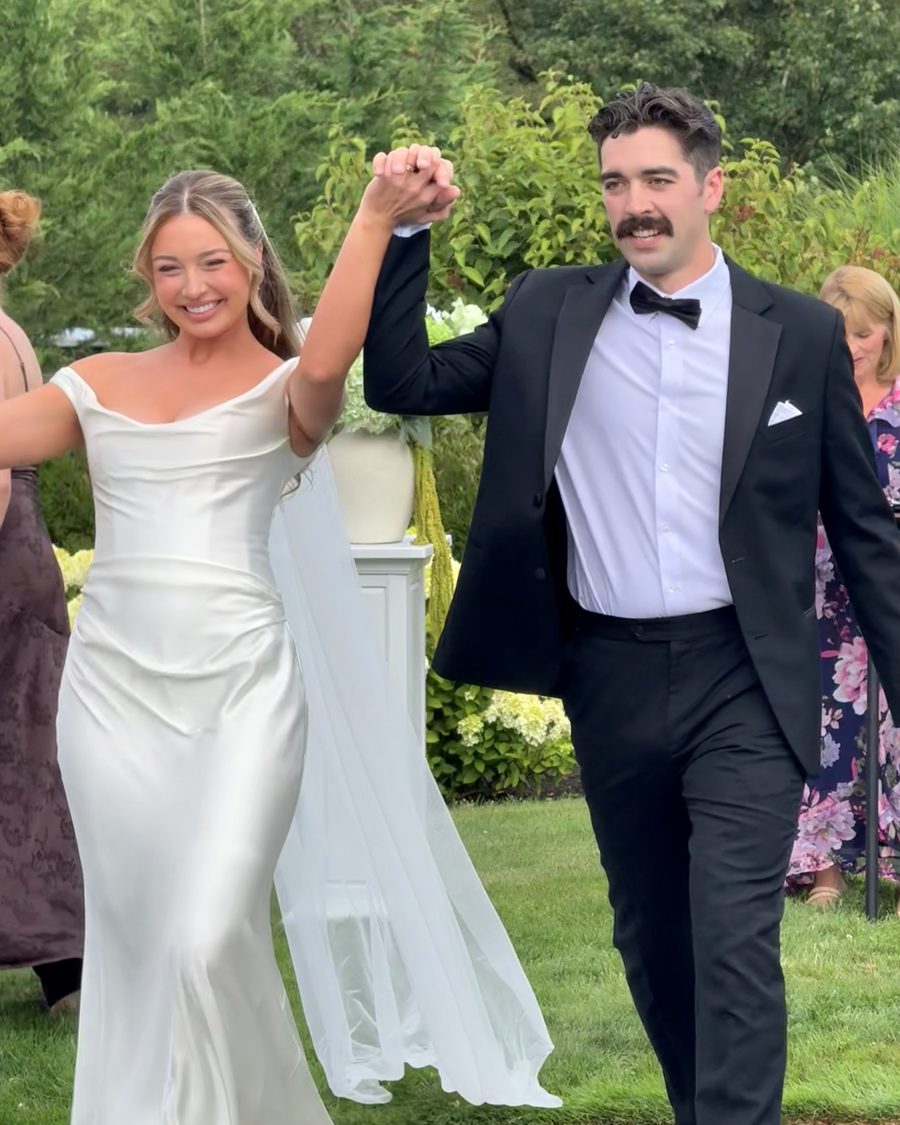 A couple walking back up the aisle hand in hand, arms raised