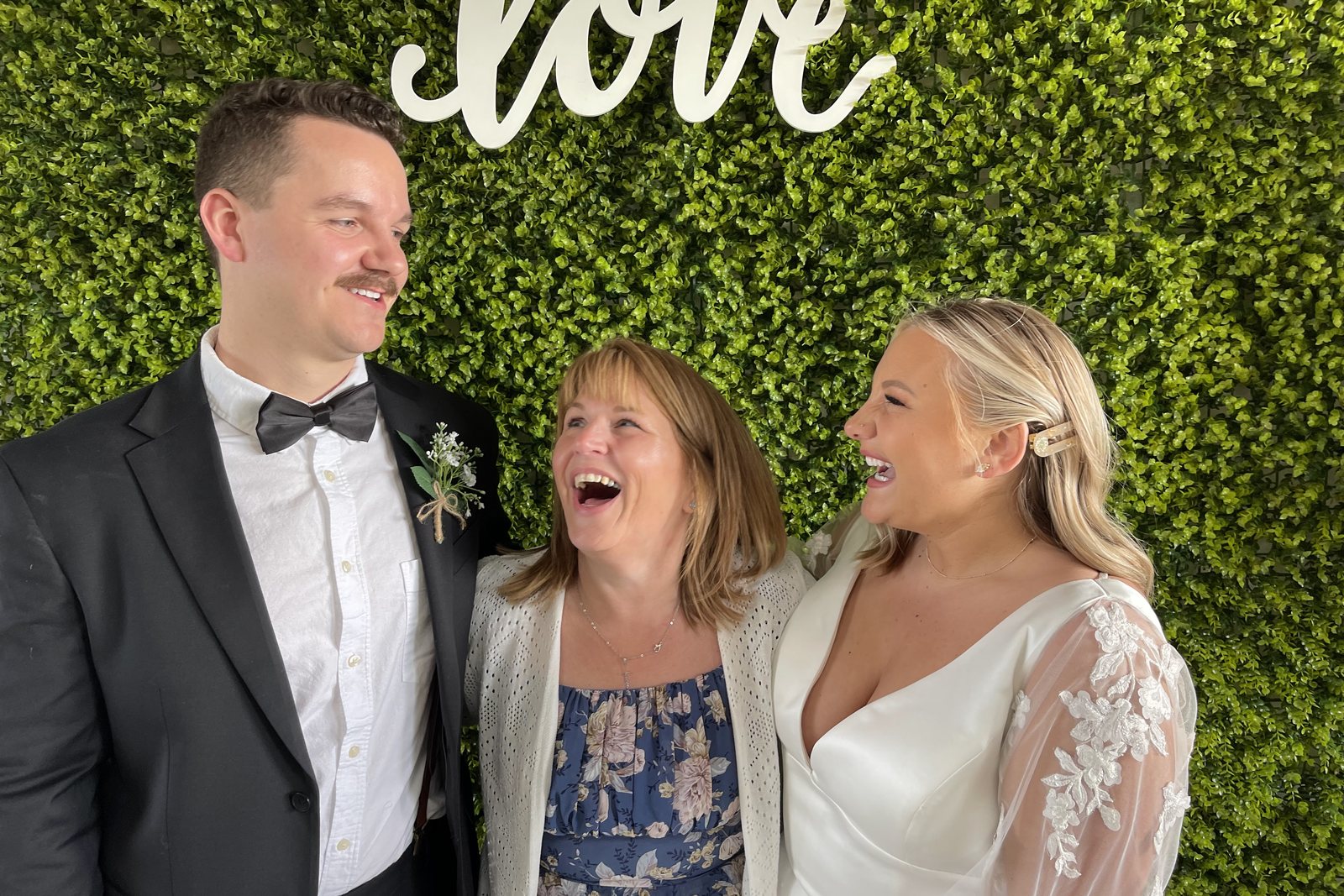 Rhonda laughing with a couple in front of a greenery wall